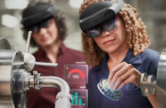 仕事で HoloLens デバイスを使用している 1 人の女性と、それを見守る別の同僚女性。