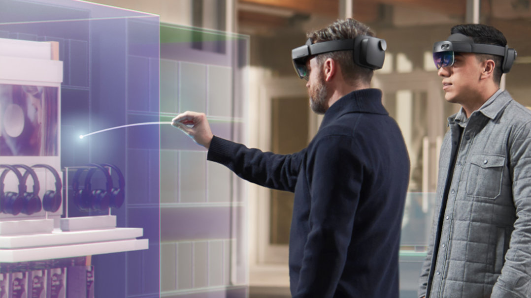 Ein Mann benutzt ein HoloLens-Gerät, um mit einem Gegenstand aus dem Inventar zu interagieren, während sein Kollege zuschaut.