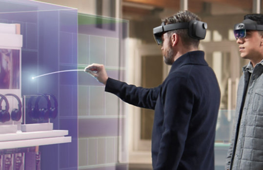 A man uses a HoloLens device to interact with an inventory item, while his co-worker looks on.