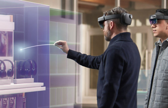 A man uses a HoloLens device to interact with an inventory item, while his coworker looks on.