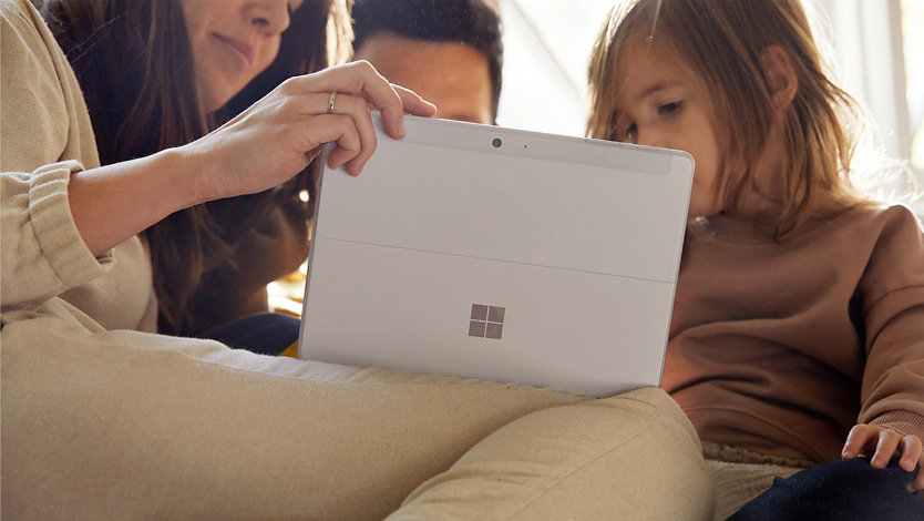 Parents look at a Surface device with their child.