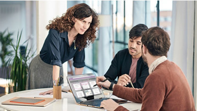 Tres personas mirando archivos en una sola Surface Laptop abierta en un escritorio.