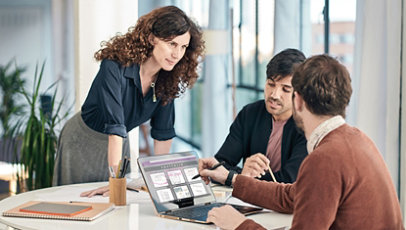 Tres personas en una reunión de negocios hablando y mirando una computadora portátil Surface.