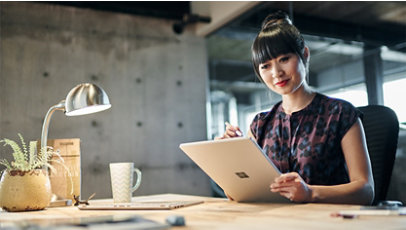 Una mujer sonriente usa un lápiz delgado con una computadora portátil Surface en una oficina moderna.