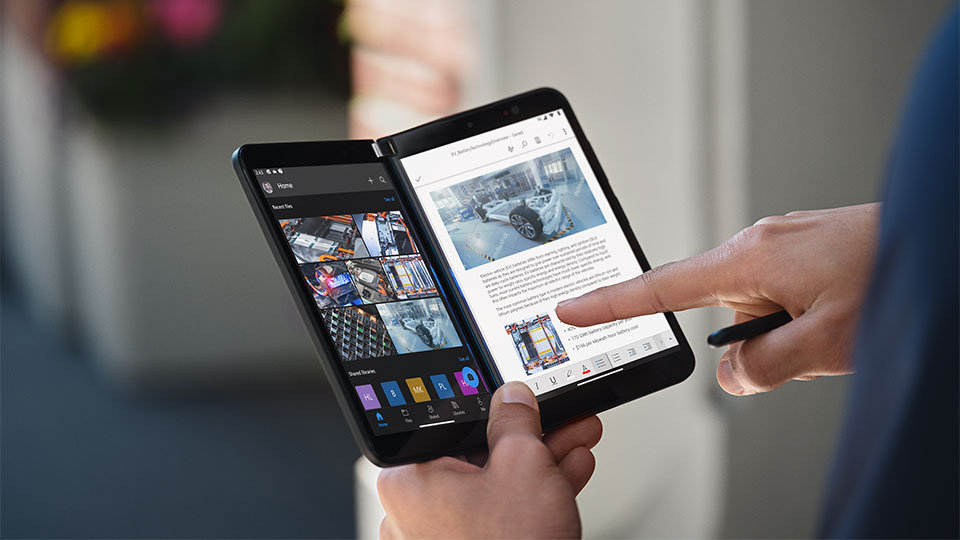 Un dispositivo Surface Duo per le aziende nella mano di una persona, aperto come un libro. Un dito indica lo schermo.