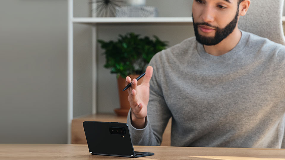 Una persona seduta a un tavolo sul quale è posato un dispositivo Surface Duo 2.