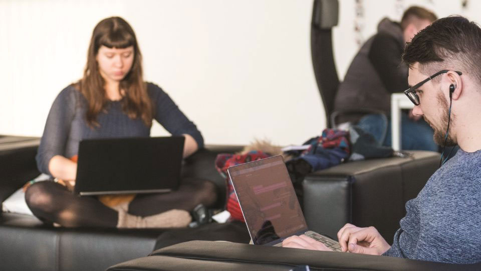 オフィスのソファに座りながらノート PC を使う人々