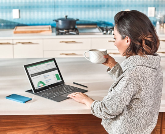 A woman uses a Surface device to review Excel charts at home.