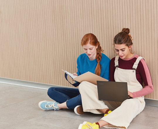 Two girls use a laptop to do schoolwork outside.