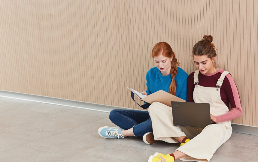 Two girls use a laptop to do schoolwork outside.