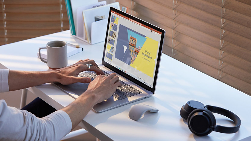 Eine Person, die an einem Surface Laptop 4 an einem Schreibtisch mit einem Headset und einer drahtlosen Maus in der Nähe arbeitet.
