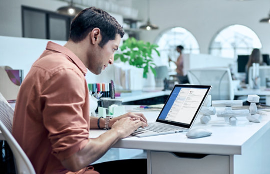 職場のデスクで Surface Book を使っている男性