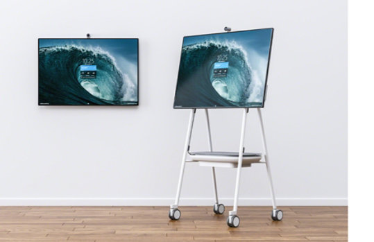 Een Surface Hub 2S aan de muur, naast een Surface Hub 2S op de mobiele Steelcase Roam-standaard