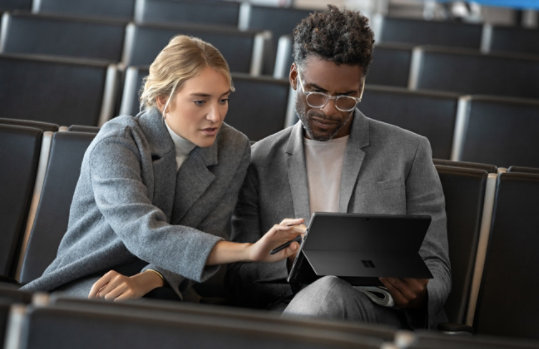 Zwei Kollegen arbeiten in einem Hörsaal an einem Microsoft-Gerät.