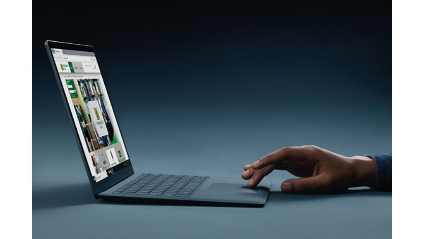 An open Surface laptop with a person's hand typing and Microsoft Edge on screen. 