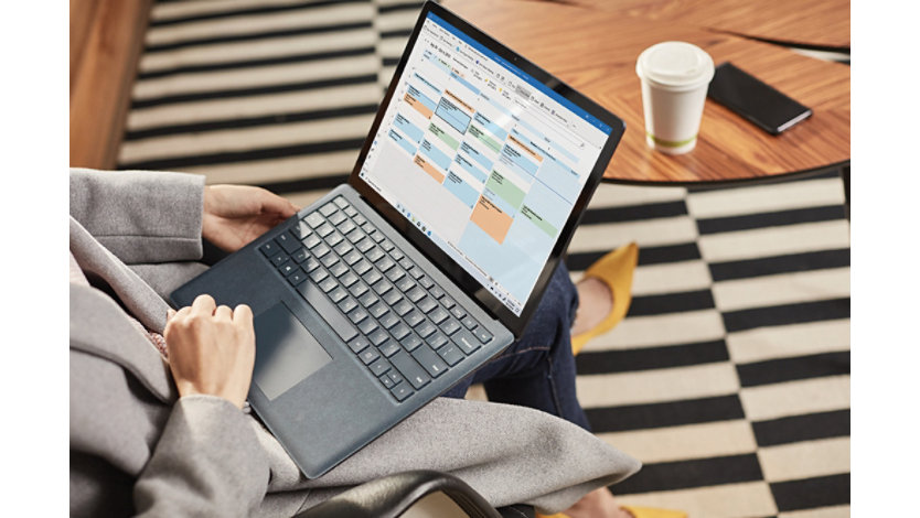 A person with an open Surface laptop on their lap and a Microsoft Outlook calendar on screen. 