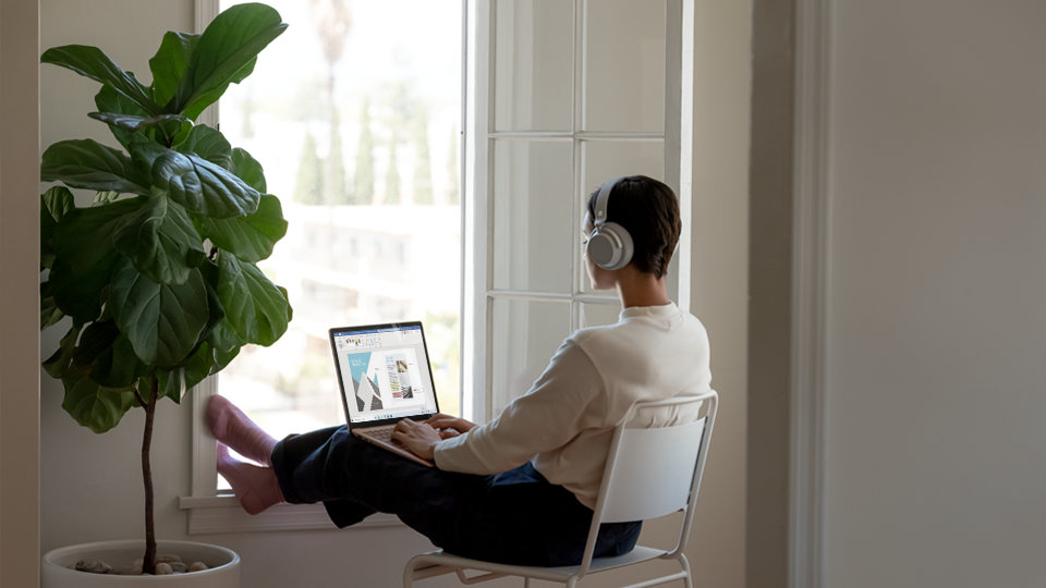 A person sits by a window doing creative work on a Surface Laptop 3.
