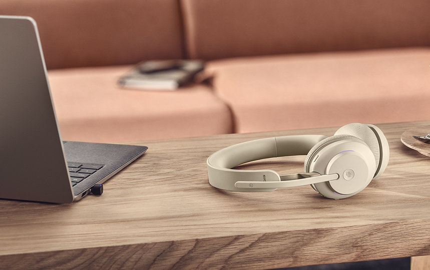 Evolve2 65 wireless headphones in beige next to a laptop and espresso.