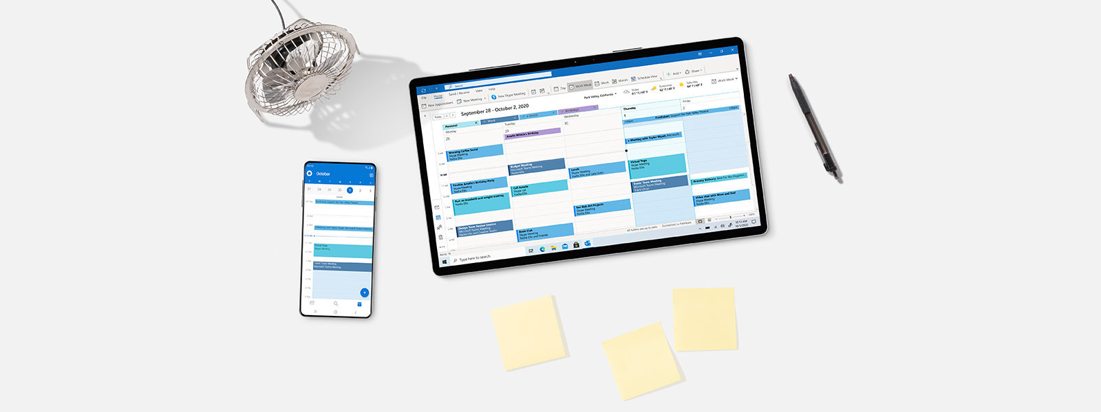 Top-Down-Ansicht eines Surface-Tablets mit Slim Pen und Smartphone auf einem Schreibtisch mit Notizen und einem Ventilator.