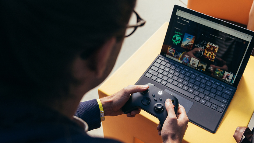 A person browses XBOX games on his Surface device with a Wireless Controller. 