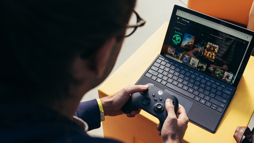 Uma pessoa bucando por jogos Xbox em seu dispositivo Surface com um comando sem fio.  