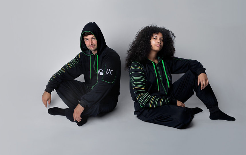 Two people seated wearing Xbox Series X Hooded Union Suits.