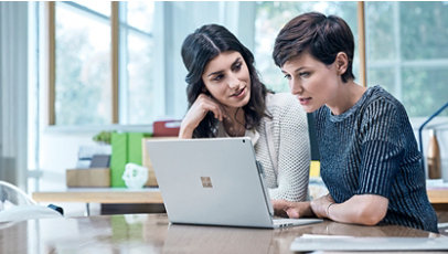 Dos personas se sientan juntas en una mesa para trabajar en una computadora portátil Surface.