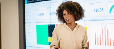 A person is speaking in front of a screen displaying various graphs and charts.