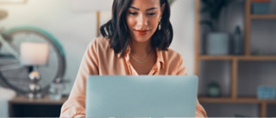 Person in an orange shirt working on a laptop in a home office setting.