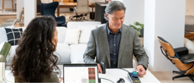 Two individuals in a business meeting with one person presenting on a laptop in a modern office setting.