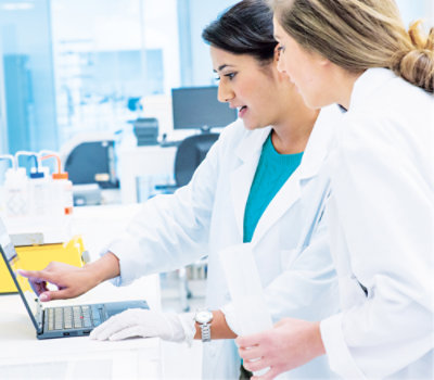 A few women in lab coats looking at a laptop.