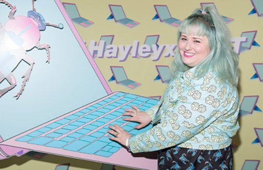 Hayley Elsaesser devant une grande découpe en forme d’ordinateur portable