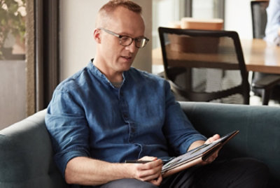 A person seated on a sofa works on a digital tablet while holding a stylus in an office setting. 