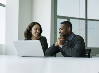 兩個人坐在筆記型電腦前，微笑討論事情