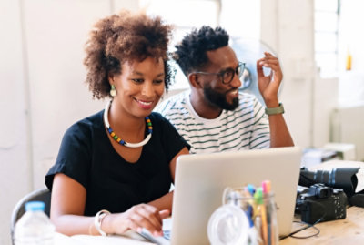 Two people at a desk with a laptop and a camera