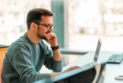 Osoba sedící u stolu a dívající se na přenosný počítač