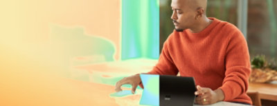 一位穿著橘色毛衣的男士坐在桌前使用電腦。