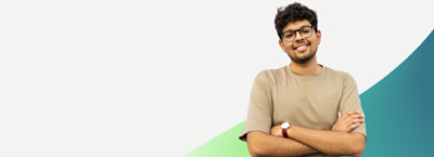 Gözlüklü ve sakallı bir kişi, beyaz ve yeşil arka planın önünde kollarını kavuşturmuş bir şekilde duruyor