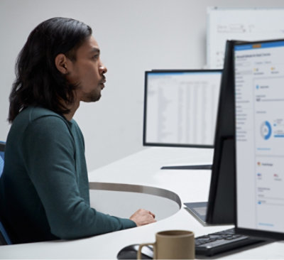 A man with long hair and a beard sitting at a desk looking at a computer screen.