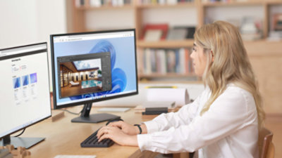 A woman is working at a desk with two computer monitors.