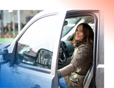 A person sits in the driver's seat of a car, smiling, with the driver's door open.