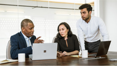 Un groupe de personnes assises autour d’une table regardent un ordinateur portable.