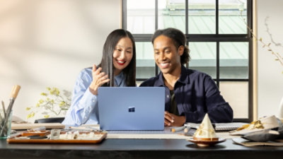 Two people sitting at a desk, smiling while looking at a blue laptop. 
