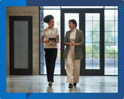 Two professionals walking through a lobby with large windows in the background.