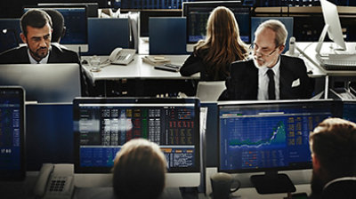 Financial services professionals viewing data charts on monitors in control room setting