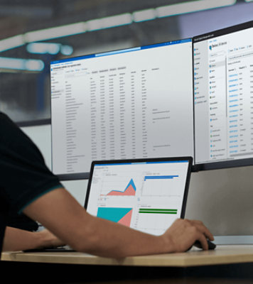 Eine Person analysiert Diagramme auf dem Laptop und Datenberichte auf zwei Monitoren.