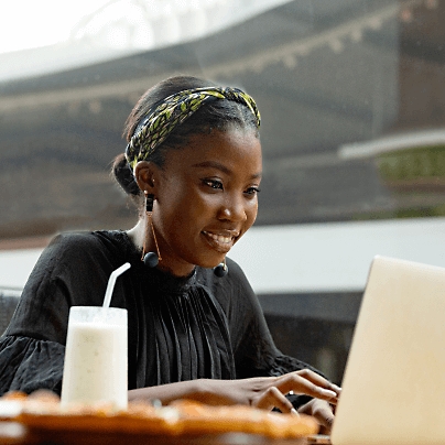 A women smiling while working on her laptop and a milk based drink by her side