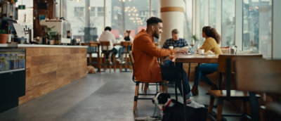 Des personnes assises dans un café et discutant, avec une personne en chemise orange à l’arrière-plan.