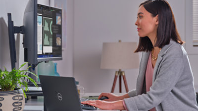 A person sitting in their home office using a laptop connected to two desktop monitors.