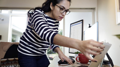 A person sitting in their home office leaning over their desk to use a tablet.